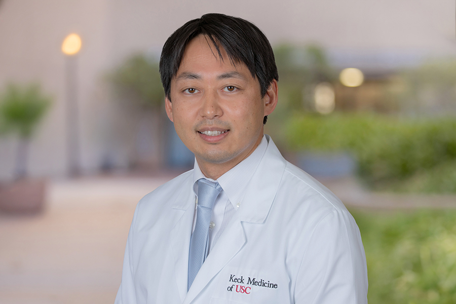 Dr. Harano Takashi stands outside in a white lab coat.