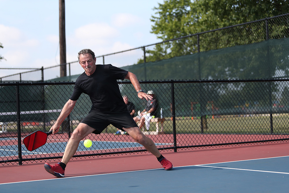 A senior man plays pickleball on sports court.
