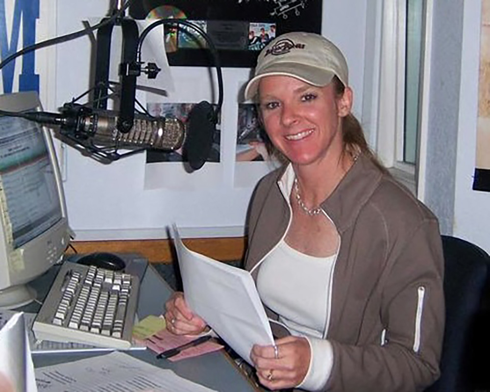 Smililng girl in baseball cap holding a script in what appears to be a radio booth.