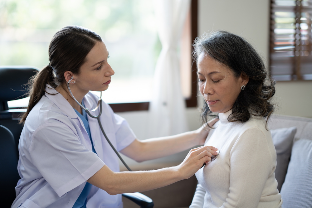 Female doctor listens to senior female patient’s heart murmur with a stethoscope.