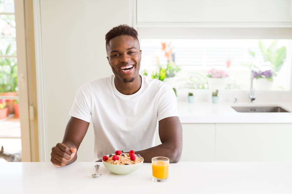 Young adult man at kitchen table eating healthy cereal and berries as breakfast.